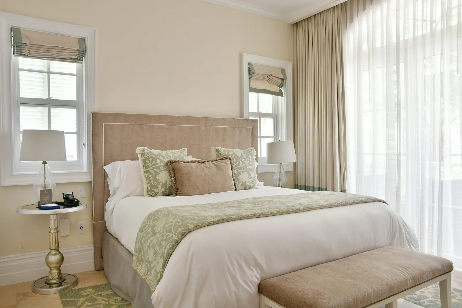 Une chambre d'amis beige et sauge, avec un banc au pied du lit