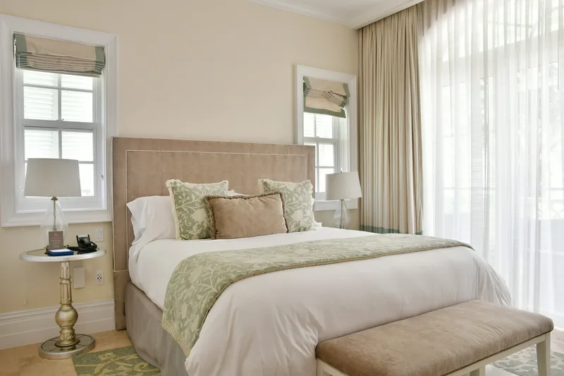 Une chambre d'amis beige et sauge, avec un banc au pied du lit
